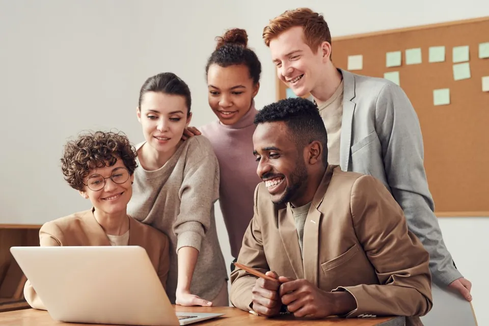 Vijf collega's kijken lachend samen naar een laptop aan een bureau